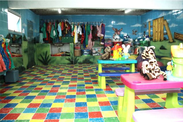 Sala com mesas infantis, brinquedos e fantasias penduradas