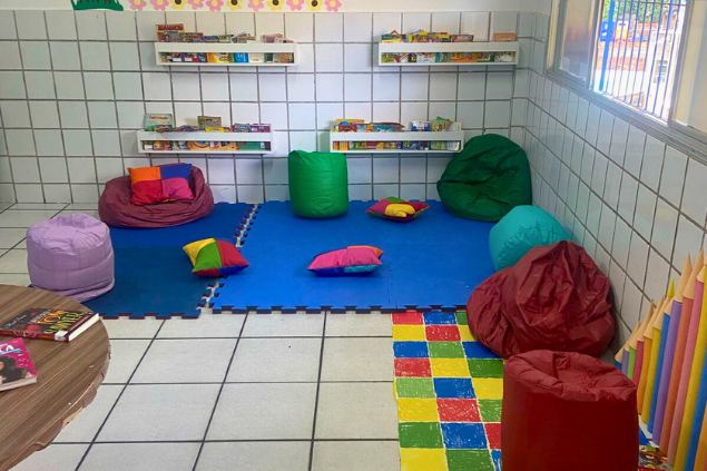 Espaço com prateleiras de livros, pufes e piso emborrachado