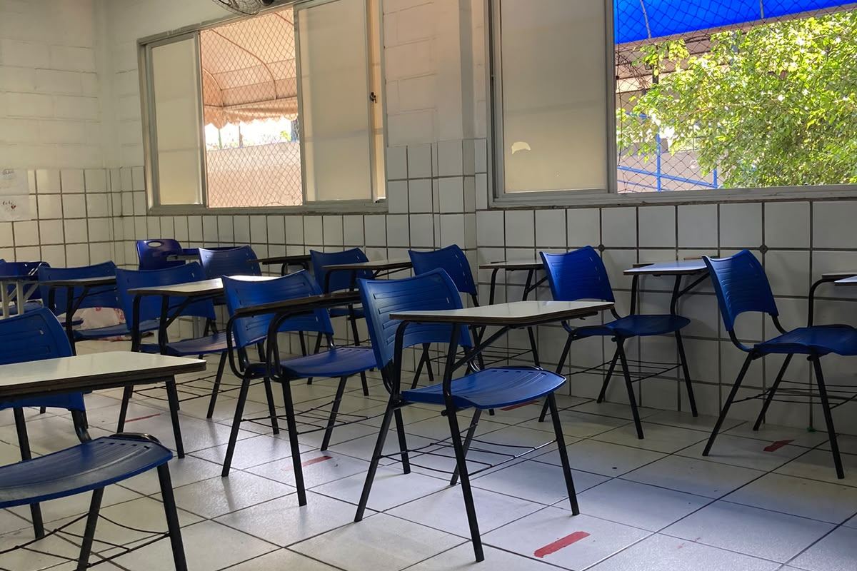 Sala de aula com carteiras azuis, janelas amplas e projetor