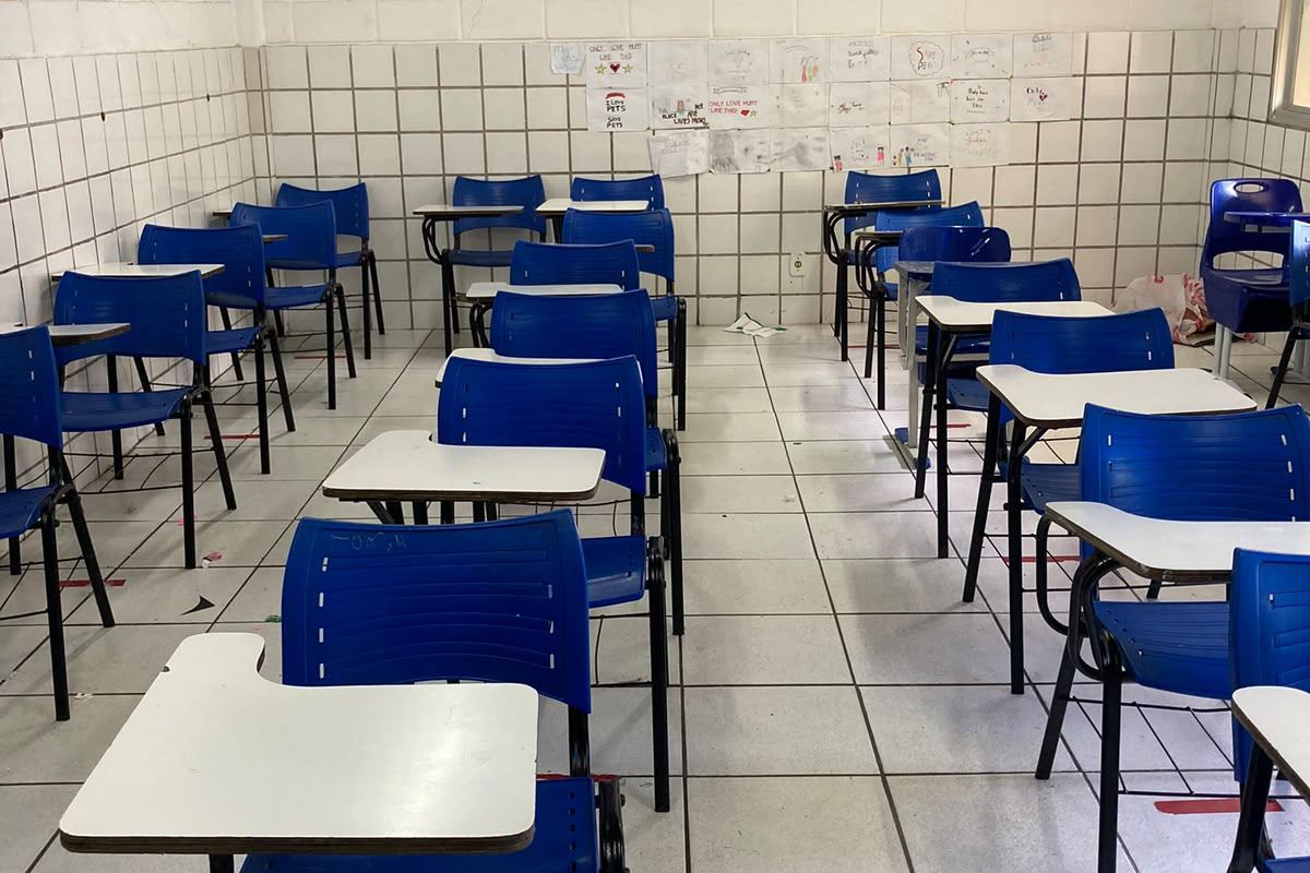 Sala de aula com fileiras de carteiras azuis e desenhos expostos na parede